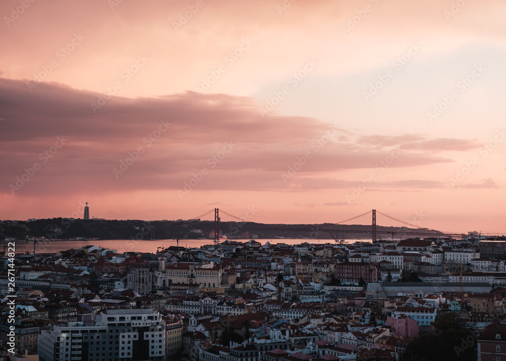view of the Alfama downtown and the 25 de Abril Bridge at a dramatic sunset in Lisbon, Portugal