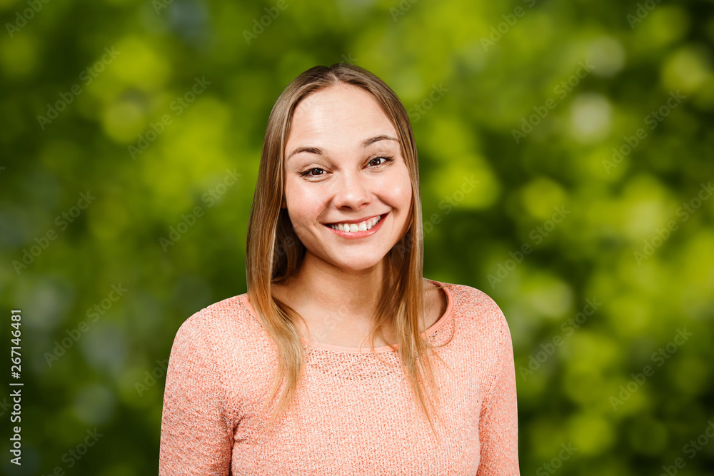 Close up portrait of beautiful smiling young woman in a beige shirt, on green bokeh background