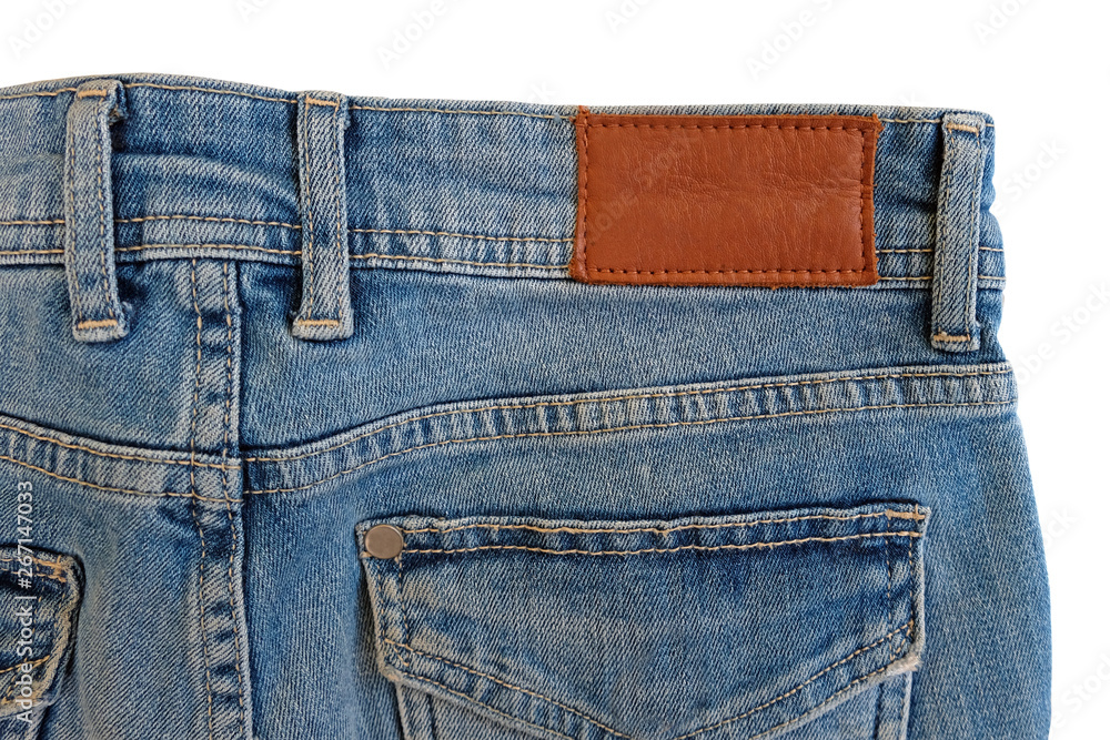 Blank brown leather label sewed on a blue jeans. Fragment of jeans trousers with brown patch