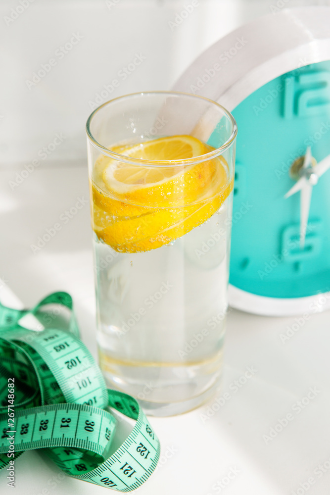 glass of water with lemon, alarm clock, measuring tape. the concept of a healthy lifestyle and weight loss glass of water with lemon, alarm clock, measuring tape. the concept of a healthy lifestyle and weight loss