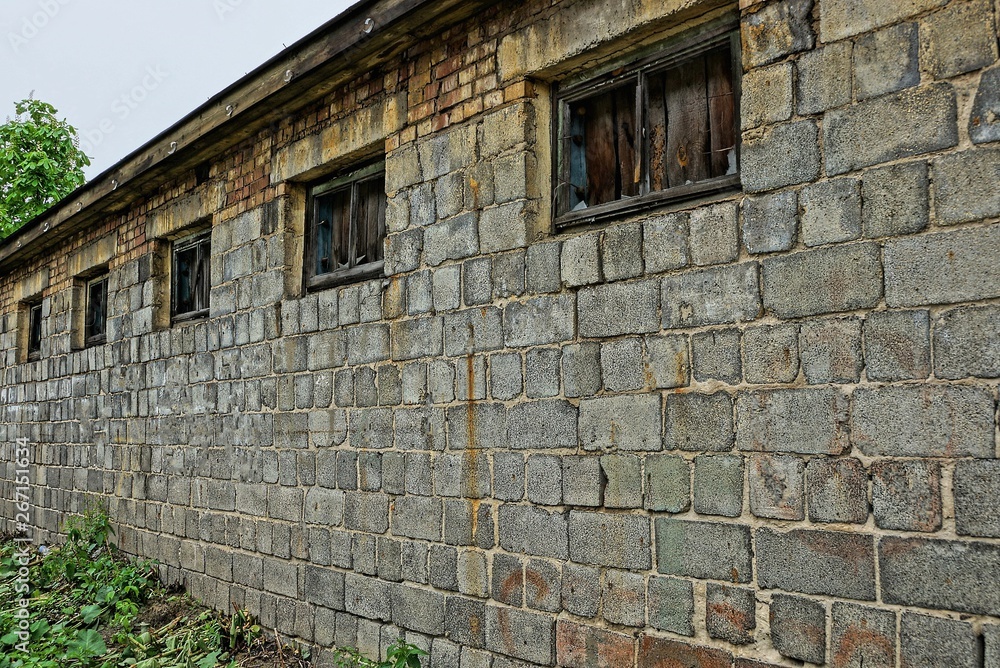 long gray brick wall of an abandoned building with broken windows