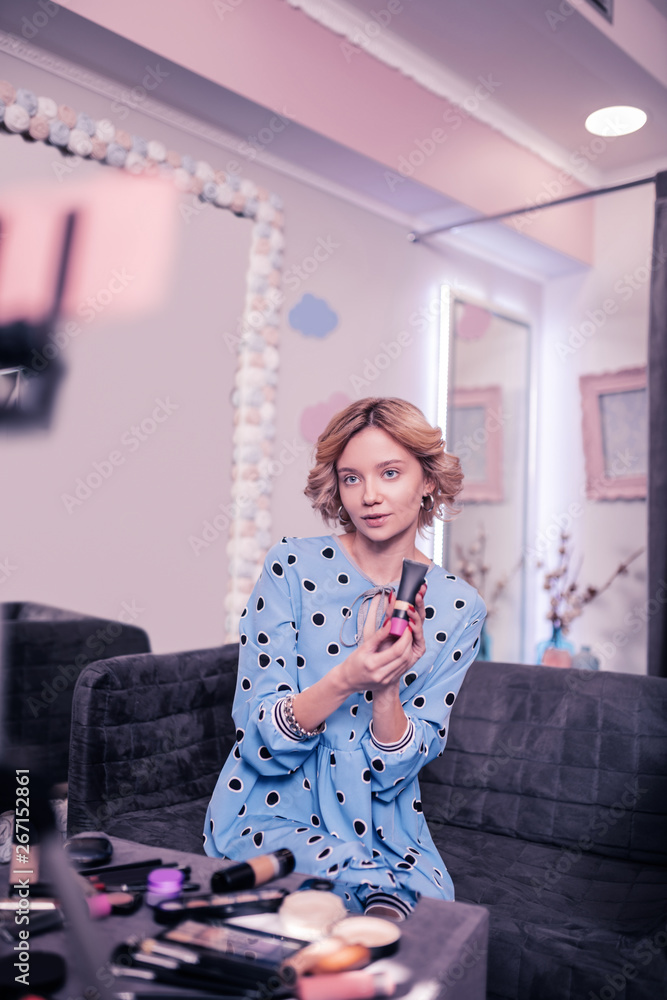 Fototapeta premium Blonde woman sitting on sofa at home filming blog about makeup