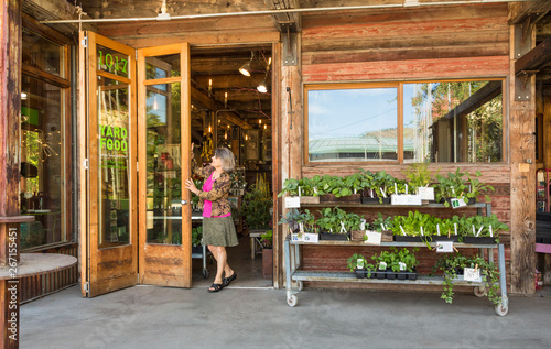 Happy, successful, middle-aged woman small business owner opening front doors of garden center shop store