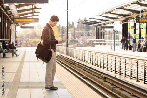 Young professional man commuter with cell phone waiting on train station platform photo