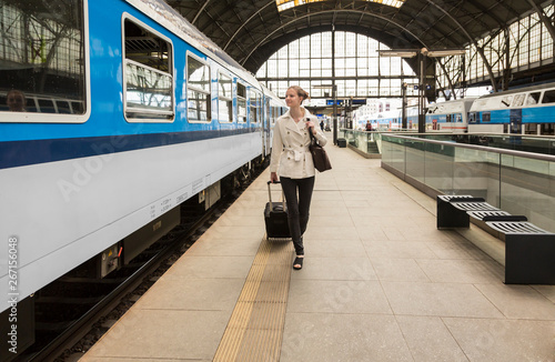 Young professional businesswoman woman traveler with roller bag suitcase boarding a train at public railway station, Prague, Czech Republic