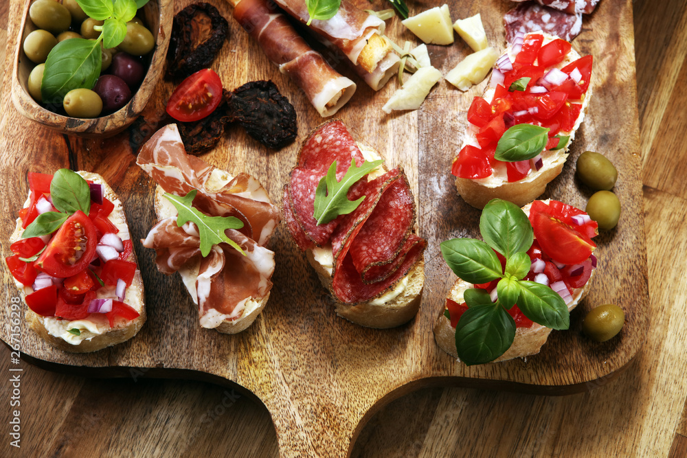 antipasto various appetizer. Cutting board with prosciutto, salami, cheese, bread and olives on dark wooden background