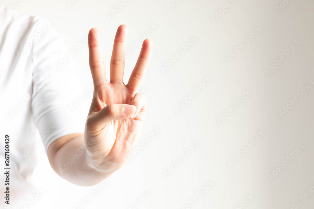 A hand showing number three by raising forefinger, middle finger and ring  finger in close-up on white background and little light. Stock Photo