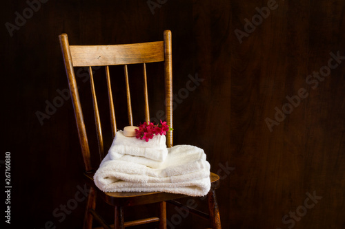 Soft white towles folded neatly on a, antique chair; towels invitingly displayed with soap and sprig of flowers photo