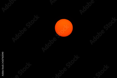 Image of the sun, orange with sun spots visible, against a black background