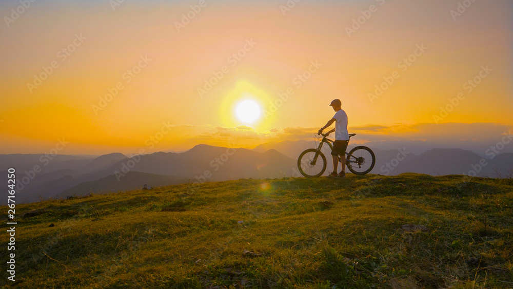 SUN FLARE: Cross country biker stands on top of a hill and watches the sunset.