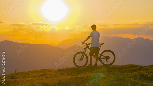 Fototapeta Naklejka Na Ścianę i Meble -  LENS FLARE: Flying towards a fit male tourist watching the sunset after cycling.
