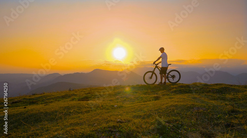 SUN FLARE: Cross country biker stands on top of a hill and watches the sunset.