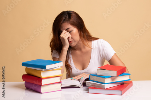 Exhausted Asian woman got headache read a book with books on table.