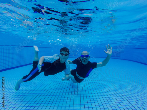A son and dad are swimming underwater in the pool, dad teaches his son to dive under water