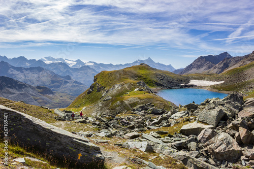 Hiking trail in Cogne valley, Aosta, Italy. Lake of Pontonnet in the high walloon of Urtier at 2800 meters of altitude. Two hikers are walking.