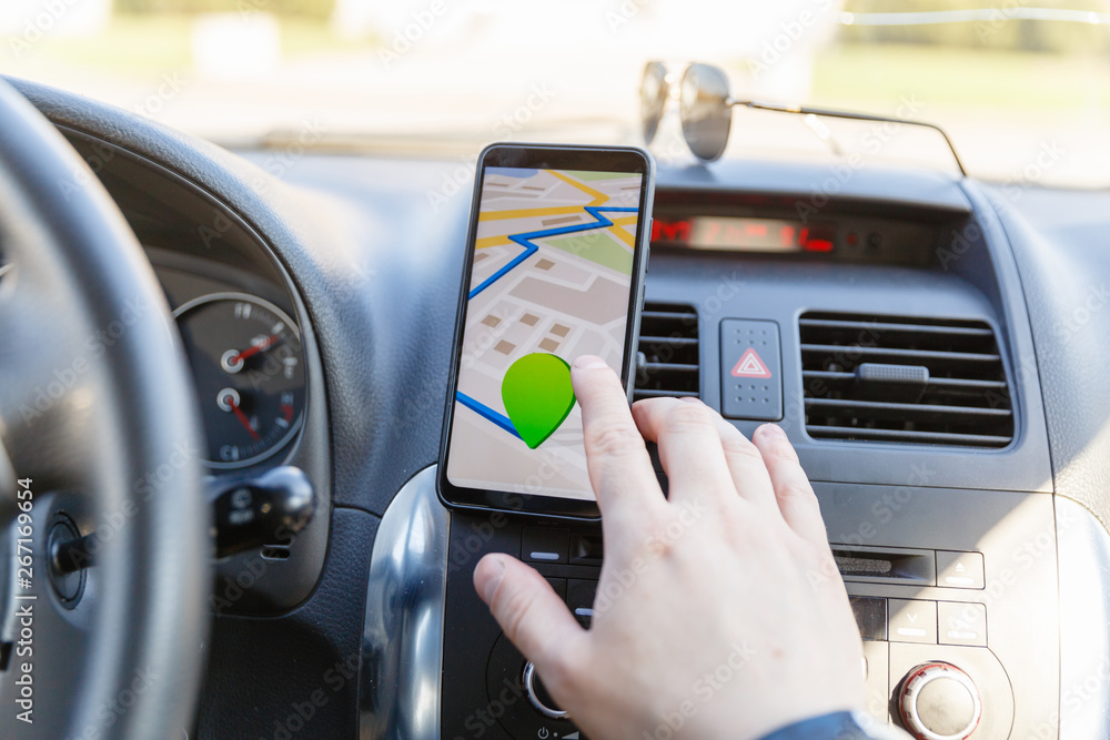 The male hand enters the coordinates on the Map on the phone against the dashboard. Black mobile phone with GPS map navigation fixed in the installation. Map application for travel. The male hand enters the coordinates on the Map on the phone against the dashboard. Black mobile phone with GPS map navigation fixed in the installation. Map application for travel.