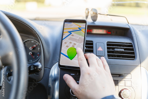 The male hand enters the coordinates on the Map on the phone against the dashboard. Black mobile phone with GPS map navigation fixed in the installation. Map application for travel.