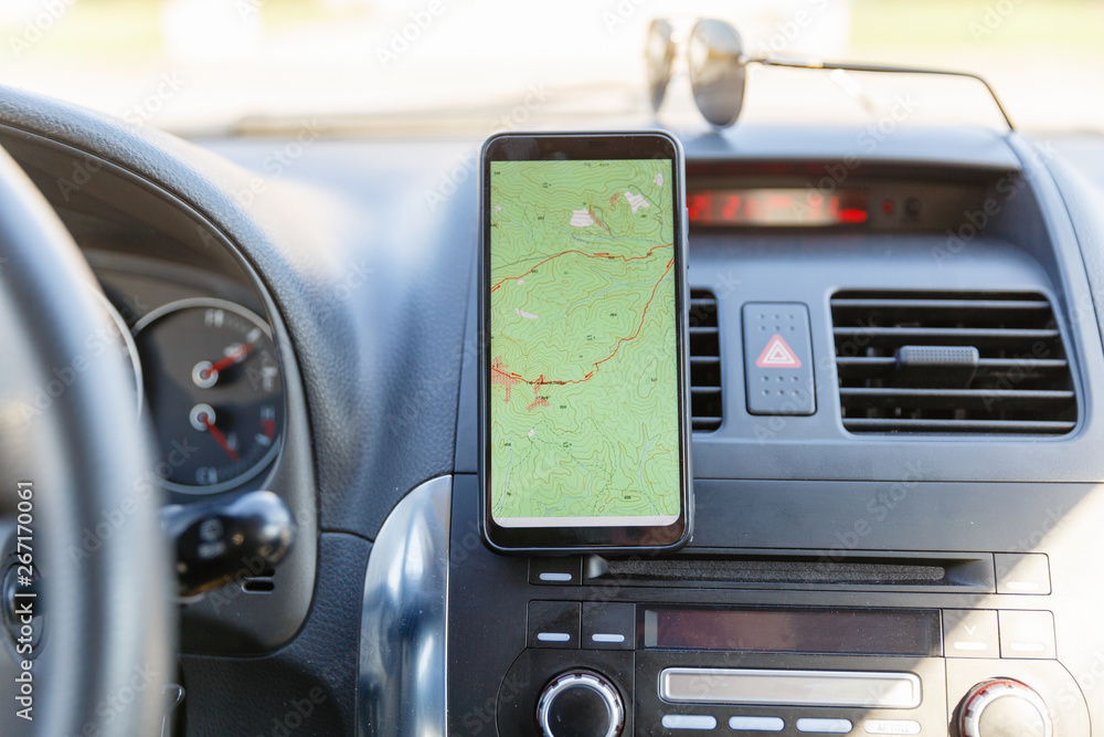 The map on the phone in the background of the dashboard. Black mobile phone with map gps navigation fixed in the mounting. App map for travel. The map on the phone in the background of the dashboard. Black mobile phone with map gps navigation fixed in the mounting. App map for travel.