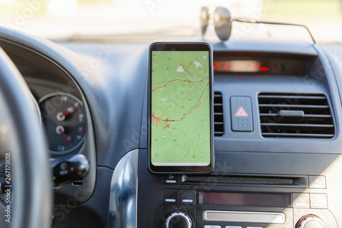 The map on the phone in the background of the dashboard. Black mobile phone with map gps navigation fixed in the mounting. App map for travel.