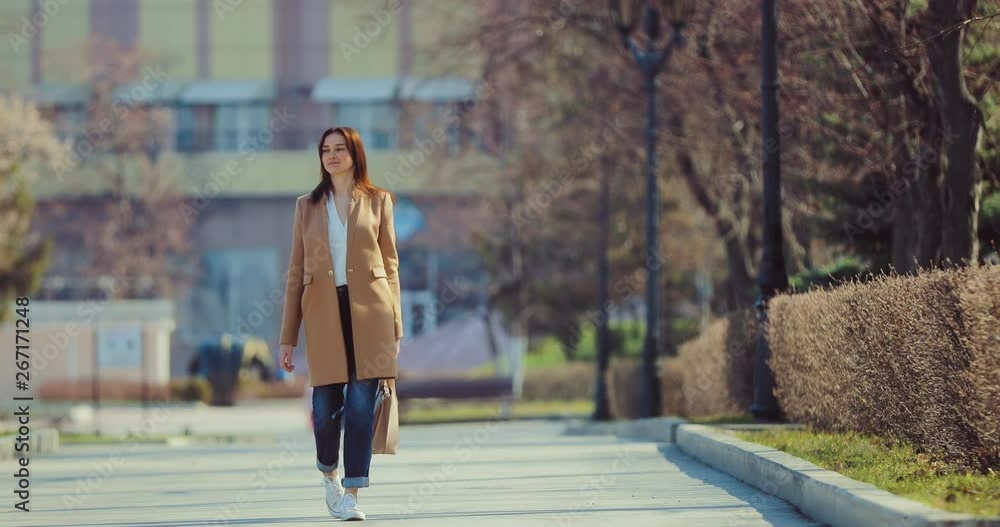 Pretty girl walking down the street in spring. Young woman walks through the spring city and smiles. Pretty girl walking down the street in spring. Young woman walks through the spring city and smiles.