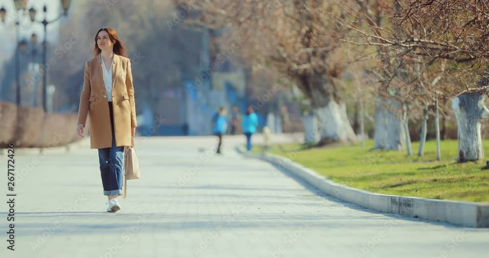 Young happy woman walks on the square in early spring. Girl is dressed stylishly, she enjoys life. Young happy woman walks on the square in early spring. Girl is dressed stylishly, she enjoys life.