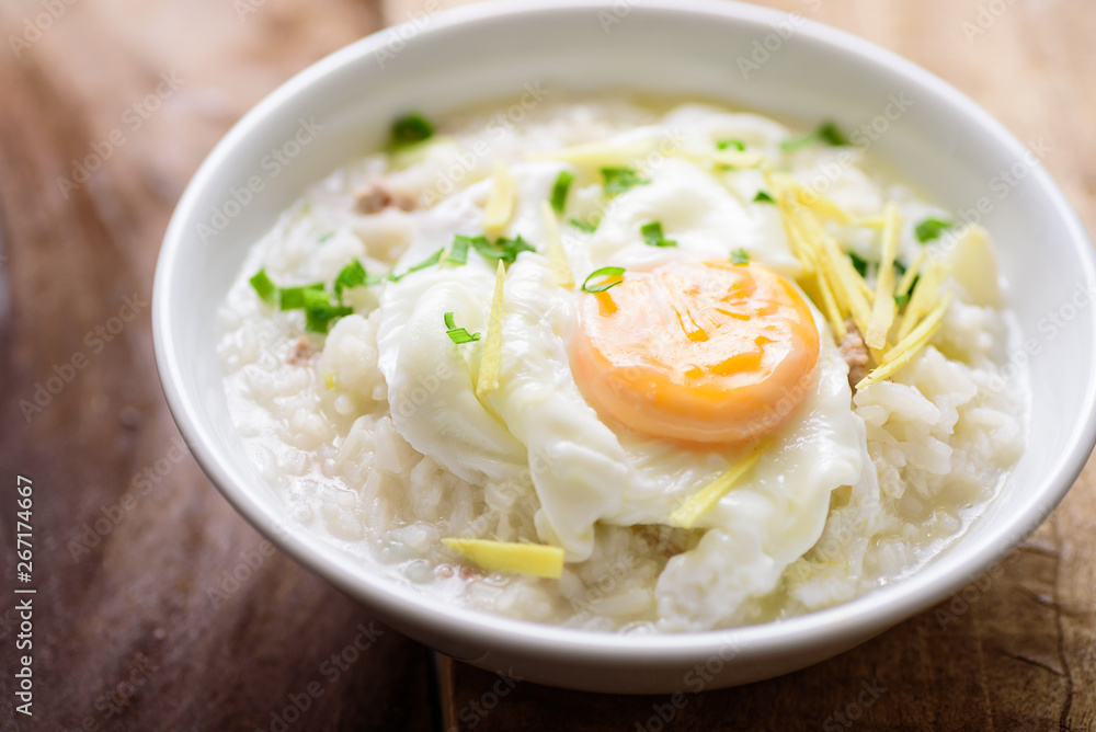 Thai rice soup or soft-boiled rice with pork and egg in the bowl on wooden background Thai rice soup or soft-boiled rice with pork and egg in the bowl on wooden background