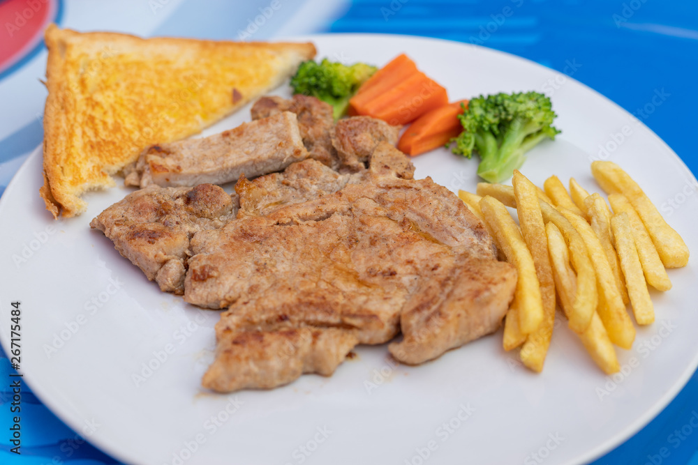 Kurobuta pork chop with vegetable and french fries in white dish. Kurobuta pork chop with vegetable and french fries in white dish.
