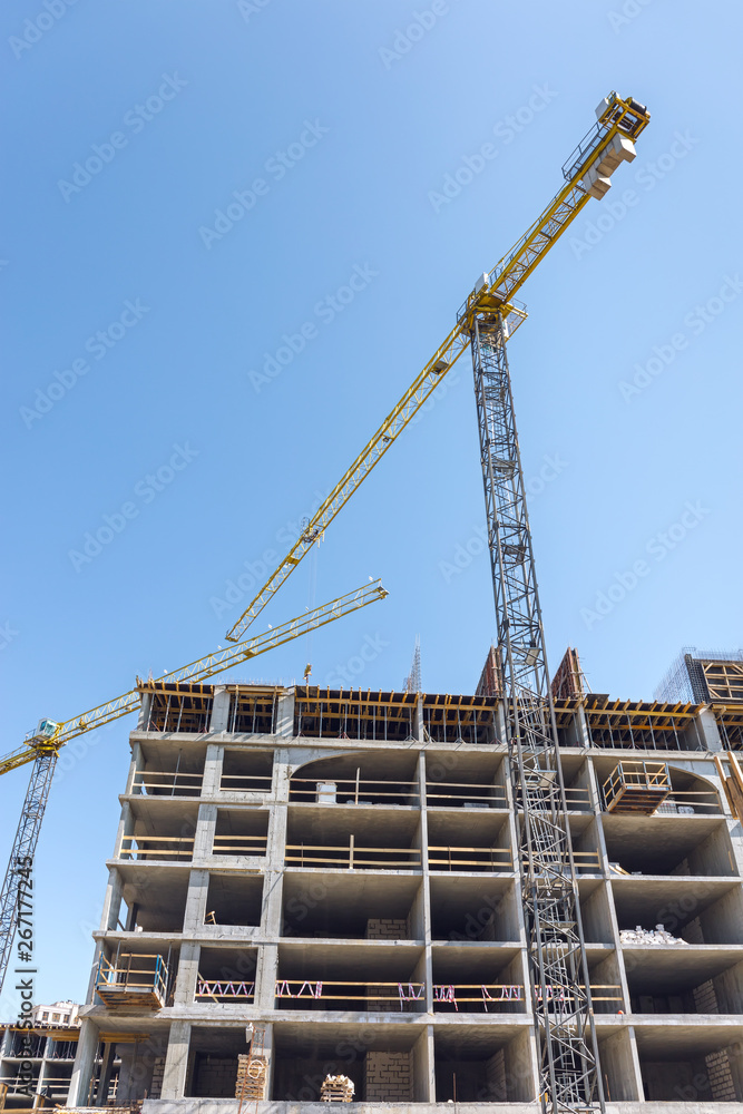 building under construction with yellow building cranes against blue sky