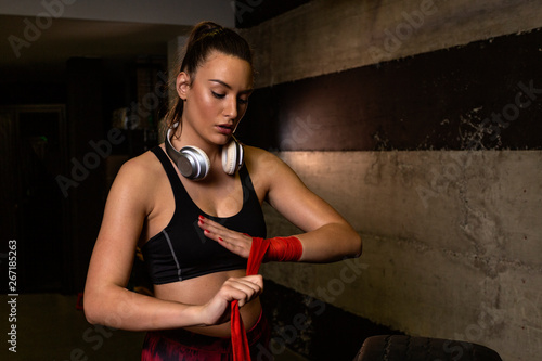 Strong woman with heaphones over her neck binds the bandage on his hand, before training photo