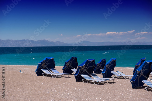 Beach on the island of Rhodes. Blue umbrellas and sun beds, bright blue sky and sea. Travel and vacation concept