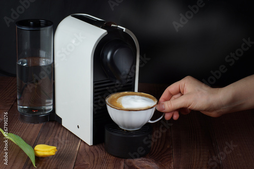 Coffee machine made a cup of cappuccino, which takes the female hand, a dark background with steam from hot coffee