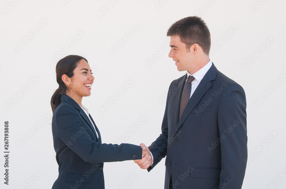 Cheerful business partners shaking hands. Young man and woman in formal suits greeting each other. Agreement or deal concept Cheerful business partners shaking hands. Young man and woman in formal suits greeting each other. Agreement or deal concept