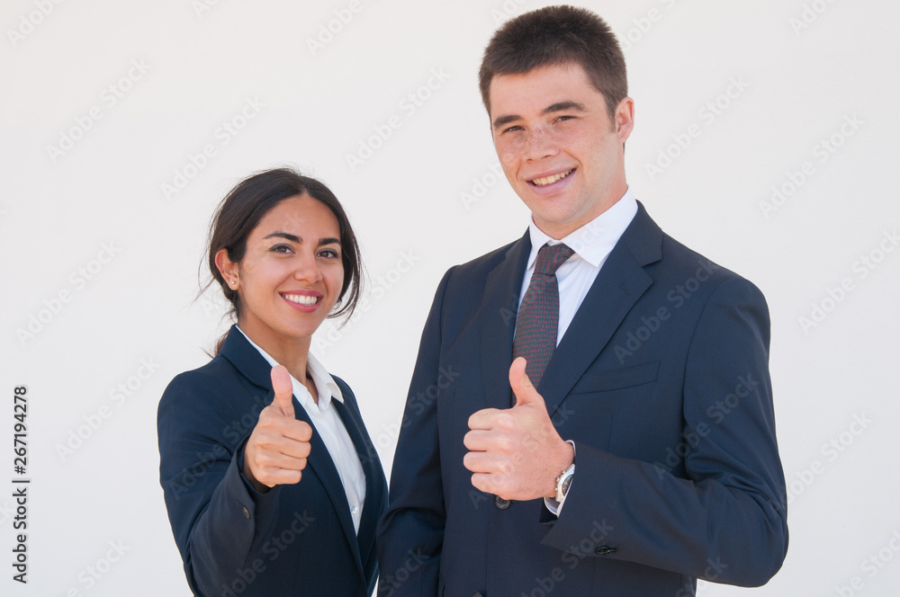 Positive confident business colleagues showing thumbs up. Young man and woman in formal jackets smiling at camera and expressing approval. Successful career concept Positive confident business colleagues showing thumbs up. Young man and woman in formal jackets smiling at camera and expressing approval. Successful career concept