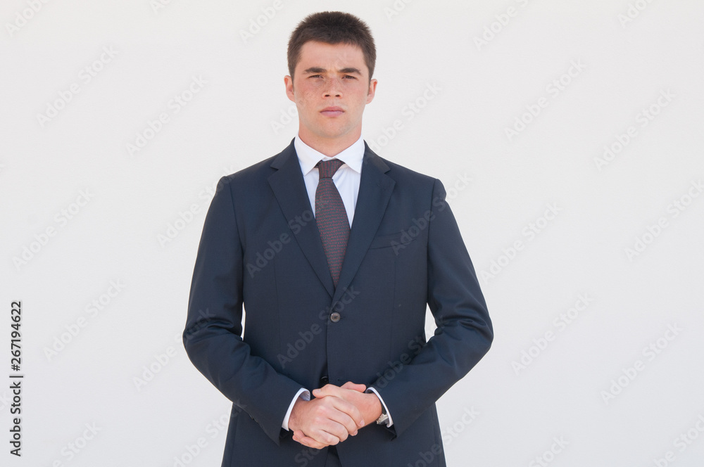 Serious office worker with clasped hands standing for camera. Portrait of young man in formal jacket and tie. Business portrait concept Serious office worker with clasped hands standing for camera. Portrait of young man in formal jacket and tie. Business portrait concept