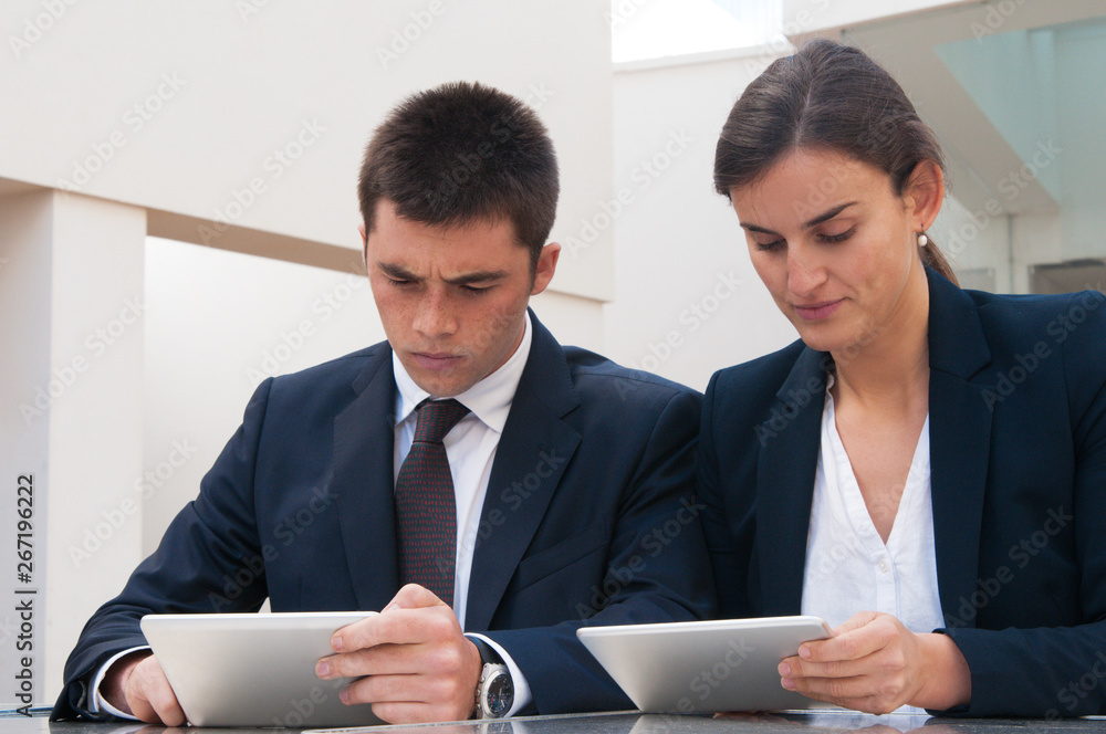 Serious business people working on tablet computers at desk. Business man and woman wearing formal clothes and sitting at cafe table. Technology in business concept. Front view. Serious business people working on tablet computers at desk. Business man and woman wearing formal clothes and sitting at cafe table. Technology in business concept. Front view.