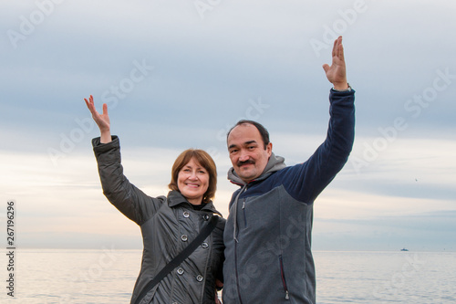 A man and a woman standing nearby raised their hands in greeting. Sea and sky in the background.