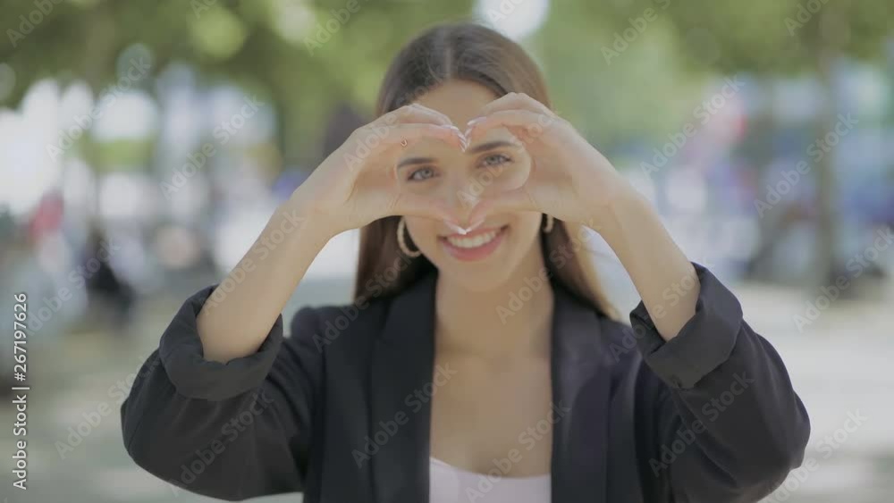 Girl showing hand heart and smiling at camera. Beautiful happy young woman showing hand heart gesture and blowing kiss outdoor. Love concept Girl showing hand heart and smiling at camera. Beautiful happy young woman showing hand heart gesture and blowing kiss outdoor. Love concept