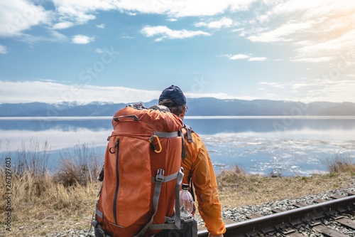 Tourist Hiking with an orange backpack is on the old railway at the foot of the mountain. Travel to lake Baikal