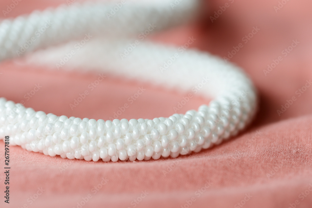 White beaded necklace on a textile background coral color close up White beaded necklace on a textile background coral color close up