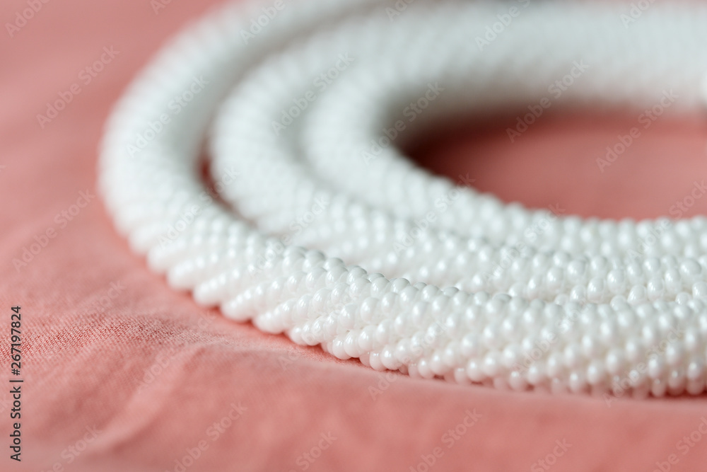 White beaded necklace on a textile background coral color close up White beaded necklace on a textile background coral color close up