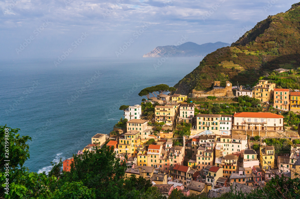 The picturesque village of Riomaggiore, Cinque Terre, Italy, on a lovely summer morning. Old traditional and colorful Italian terraced houses built at the seaside in a valley surrounded by mountains.