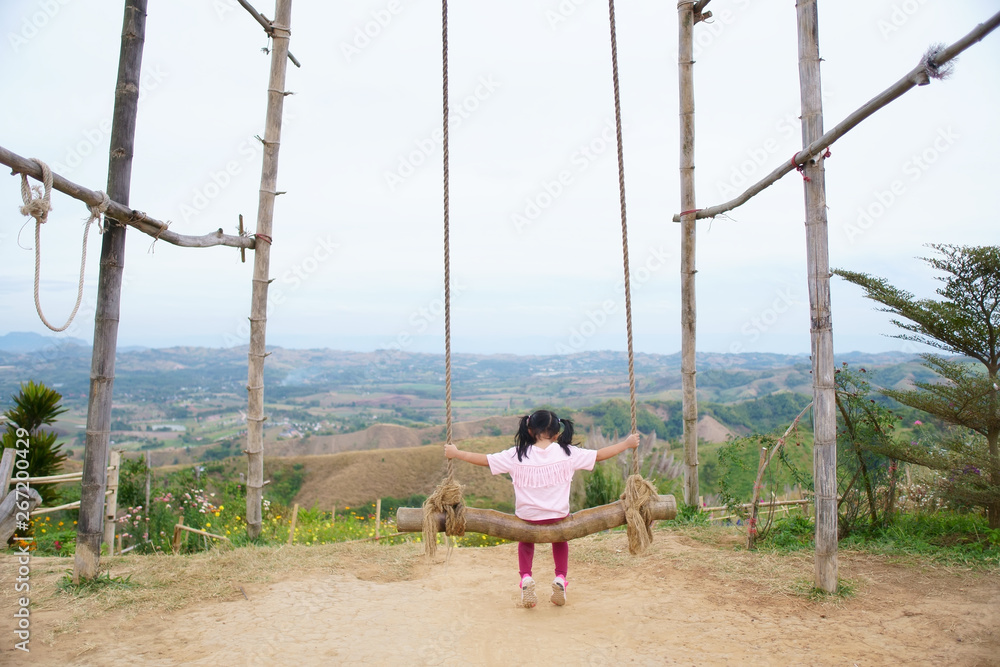 Child or back of kid girl playing wooden swing and happy fun or cheerful enjoy on nature holiday relax with landscape view in playground meadow field or amusement public park on summer travel vacation Child or back of kid girl playing wooden swing and happy fun or cheerful enjoy on nature holiday relax with landscape view in playground meadow field or amusement public park on summer travel vacation