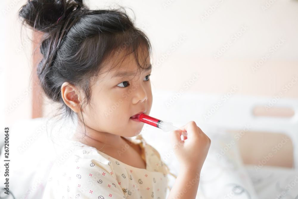 Asian child cute or kid girl Influenza sick holding and eating or taking sweet red drug or water medicine by syringe pump on bed at hospital room for pediatric patient treatment and healthcare Asian child cute or kid girl Influenza sick holding and eating or taking sweet red drug or water medicine by syringe pump on bed at hospital room for pediatric patient treatment and healthcare