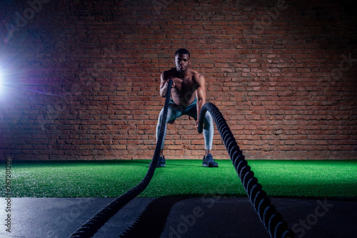 multiethnic bare sexy chest sportsmen exercising with battle ropes at the gym