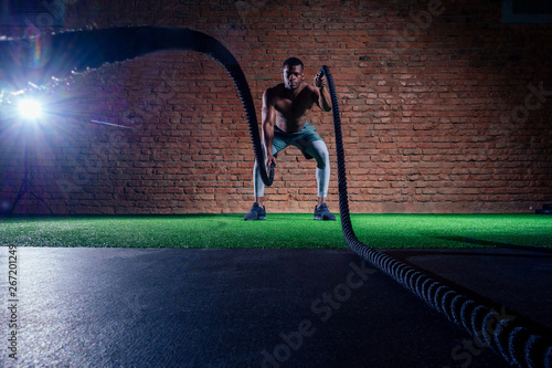 multiethnic bare sexy chest sportsmen exercising with battle ropes at the gym