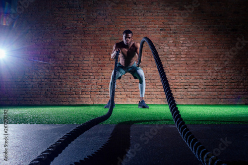 multiethnic bare sexy chest sportsmen exercising with battle ropes at the gym