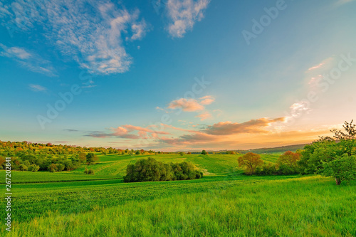 The green field with a blue sky and a few white clouds while the sun sets