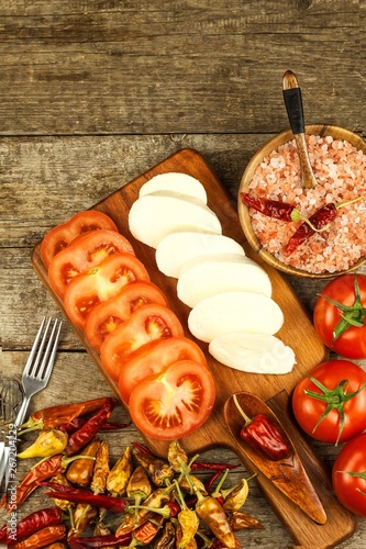 Fresh Mozzarella cheese and tomatoes onkitchen cutting board. Healthy diet food. Chili peppers with cheese. photo