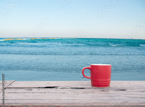 Red coffee cup on wooden table with blue sea background
