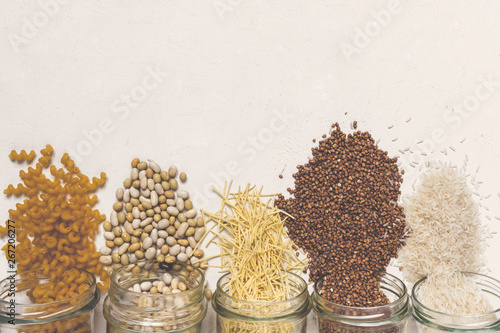 Various raw cereals, grains, beans and pasta for cooking healthy food in glass jars on a wooden table,  light  background flat,  Clean food, vegan, balanced diet,zero waste,eco friendly,plastic free
